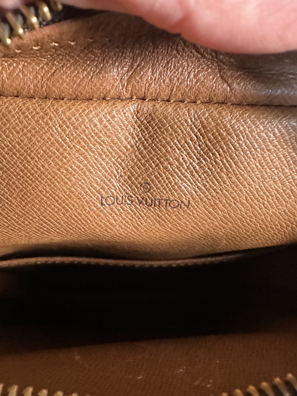 Close-up of a Louis Vuitton brown leather interior pouch showing the embossed brand name on textured Saffiano canvas.