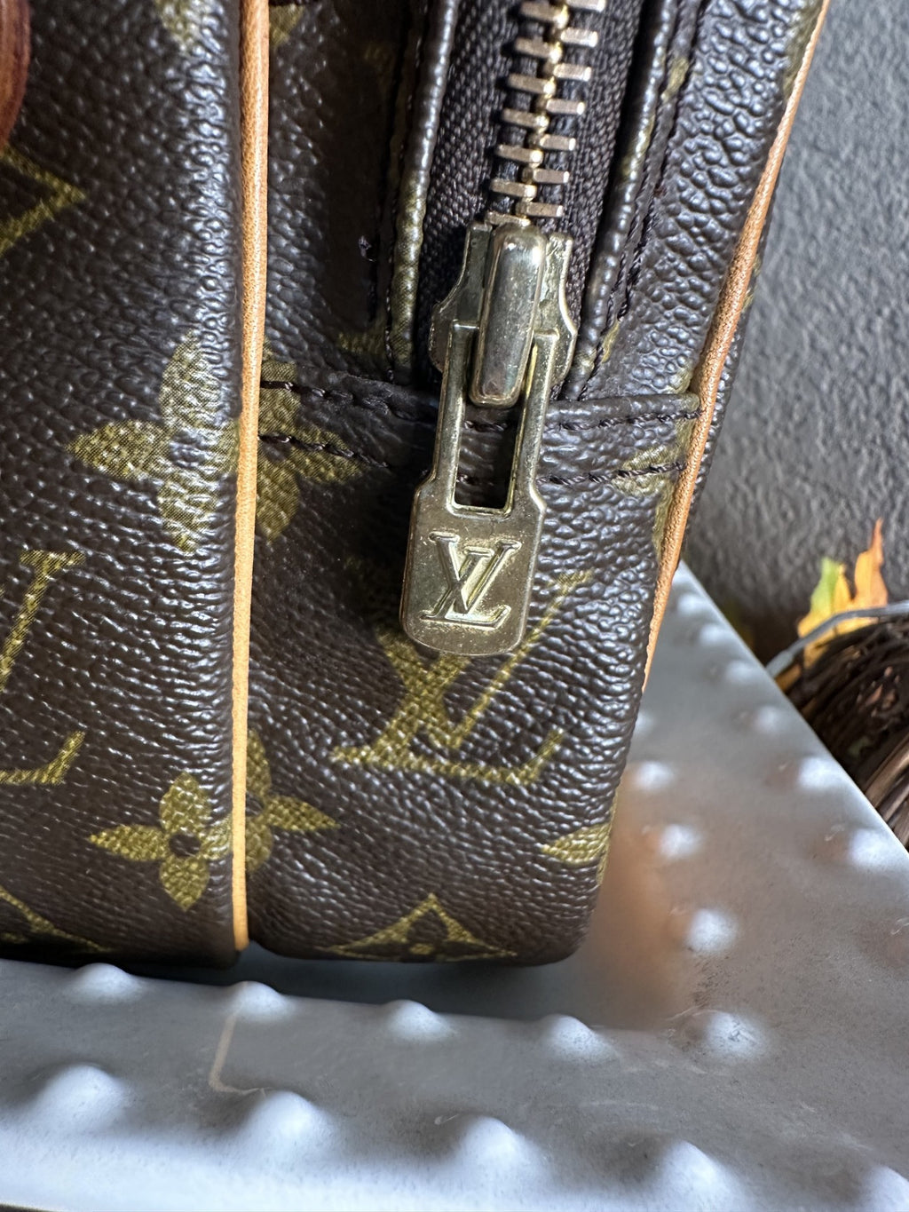 Close-up of a Louis Vuitton monogram canvas bag with a gold-tone metal zipper pull featuring the embossed LV logo.